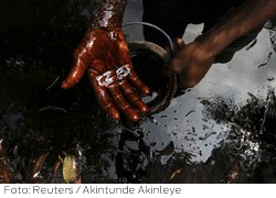 A man samples crude oil at the bank of a polluted river in Bidere community in Ogoniland in Nigeria's delta region